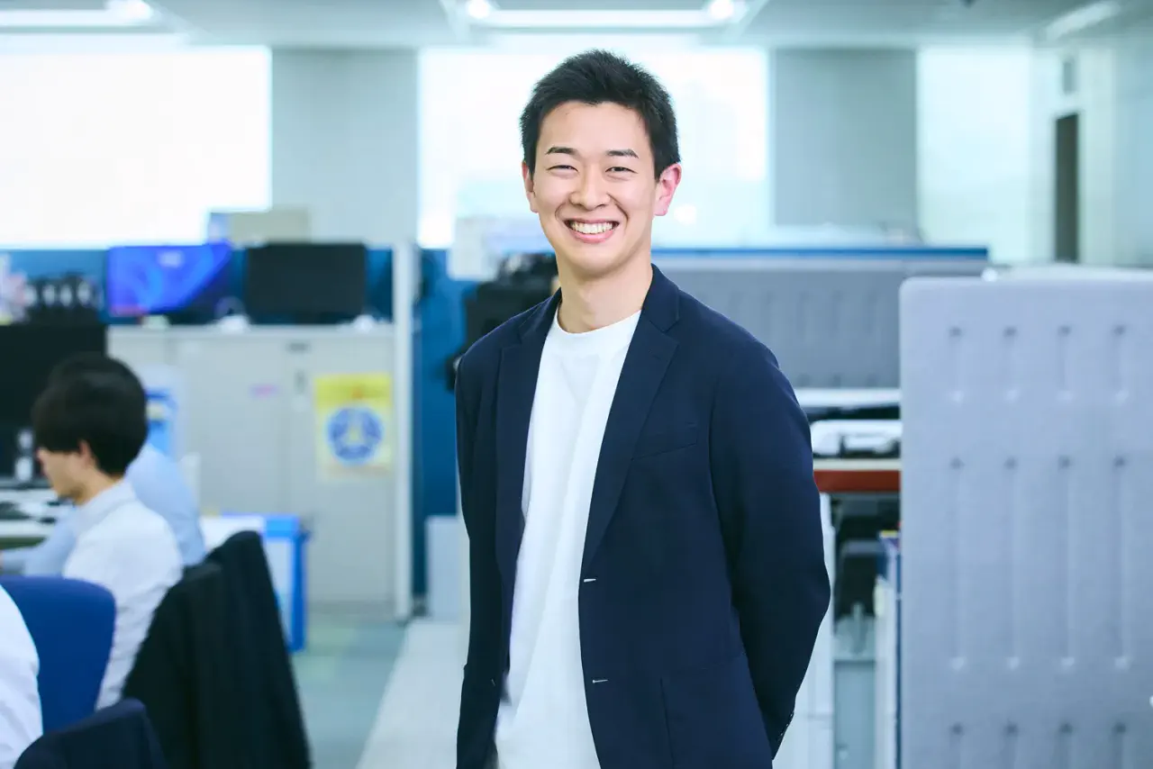 J.K. さんが執務スペース内で笑顔で正対している写真。