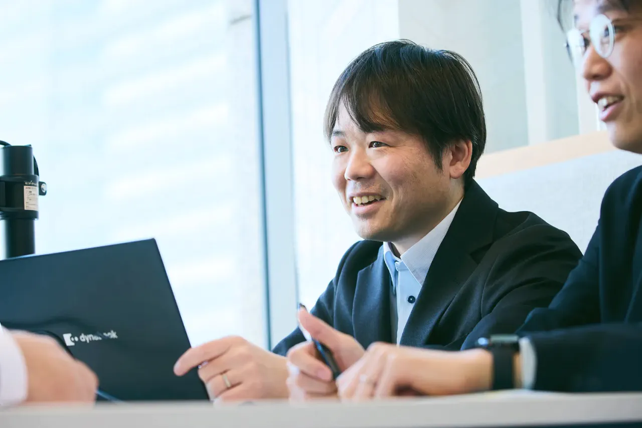 K.F. さんが男性2人と打ち合わせスペースで打ち合わせをしている写真。