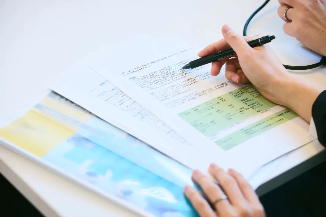 デスクの上に並べられた資料にペンでメモをしている写真。