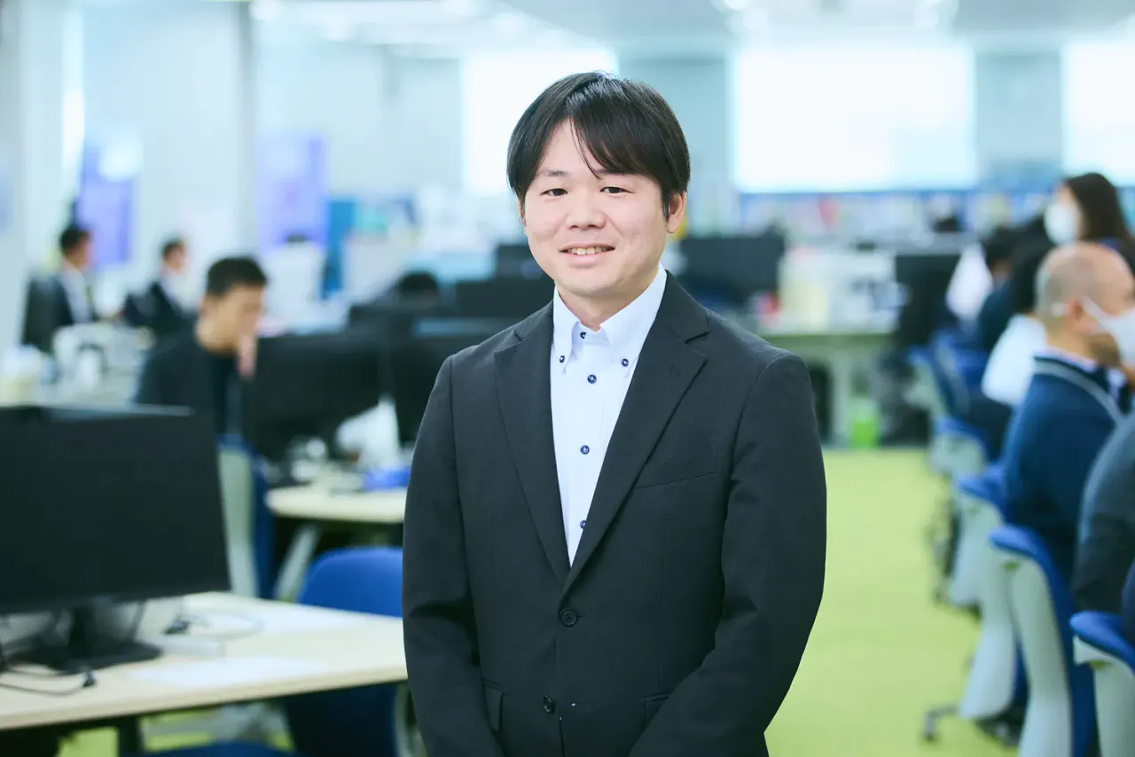 K.F. さんが執務スペース内で笑顔で正対している写真。