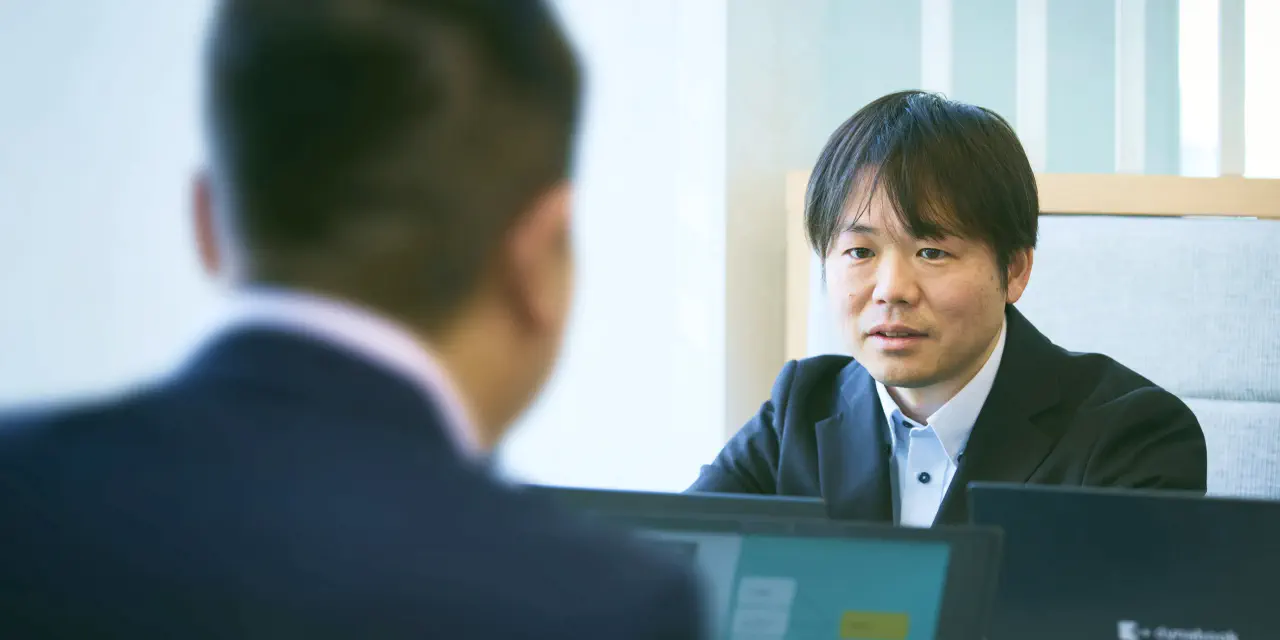 K.F.さんが打ち合わせスペースで男性社員1人と打ち合わせをしている写真。