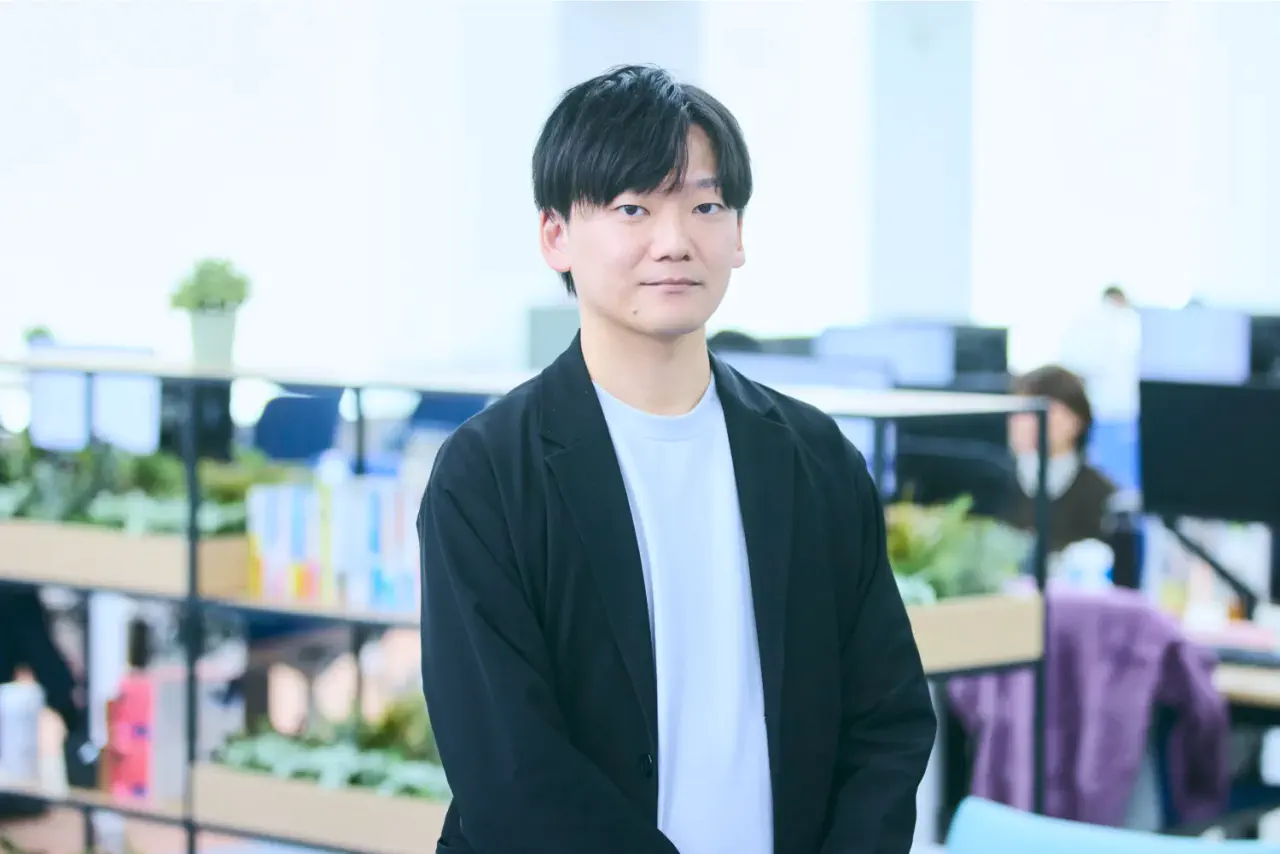 N.K. さんが執務スペース内で微笑みながら正対している写真。