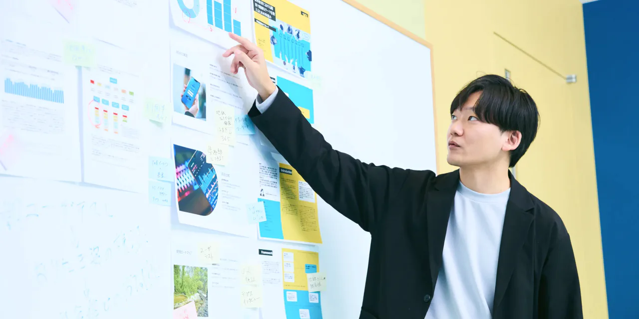 ホワイトボードを指さしながらプレゼンをする N.K.さんの写真。