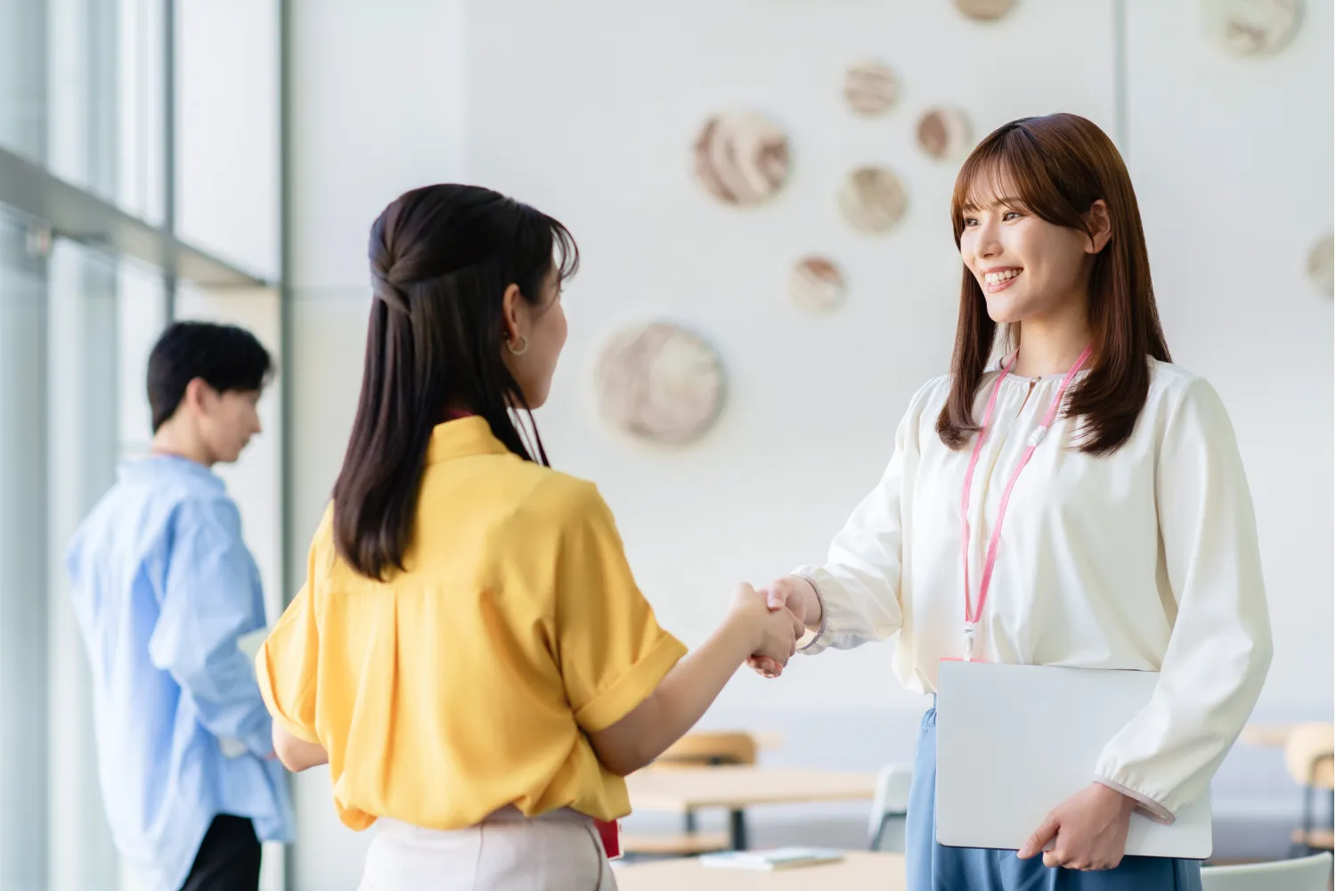 2人の女性社員が笑顔で握手をしている写真