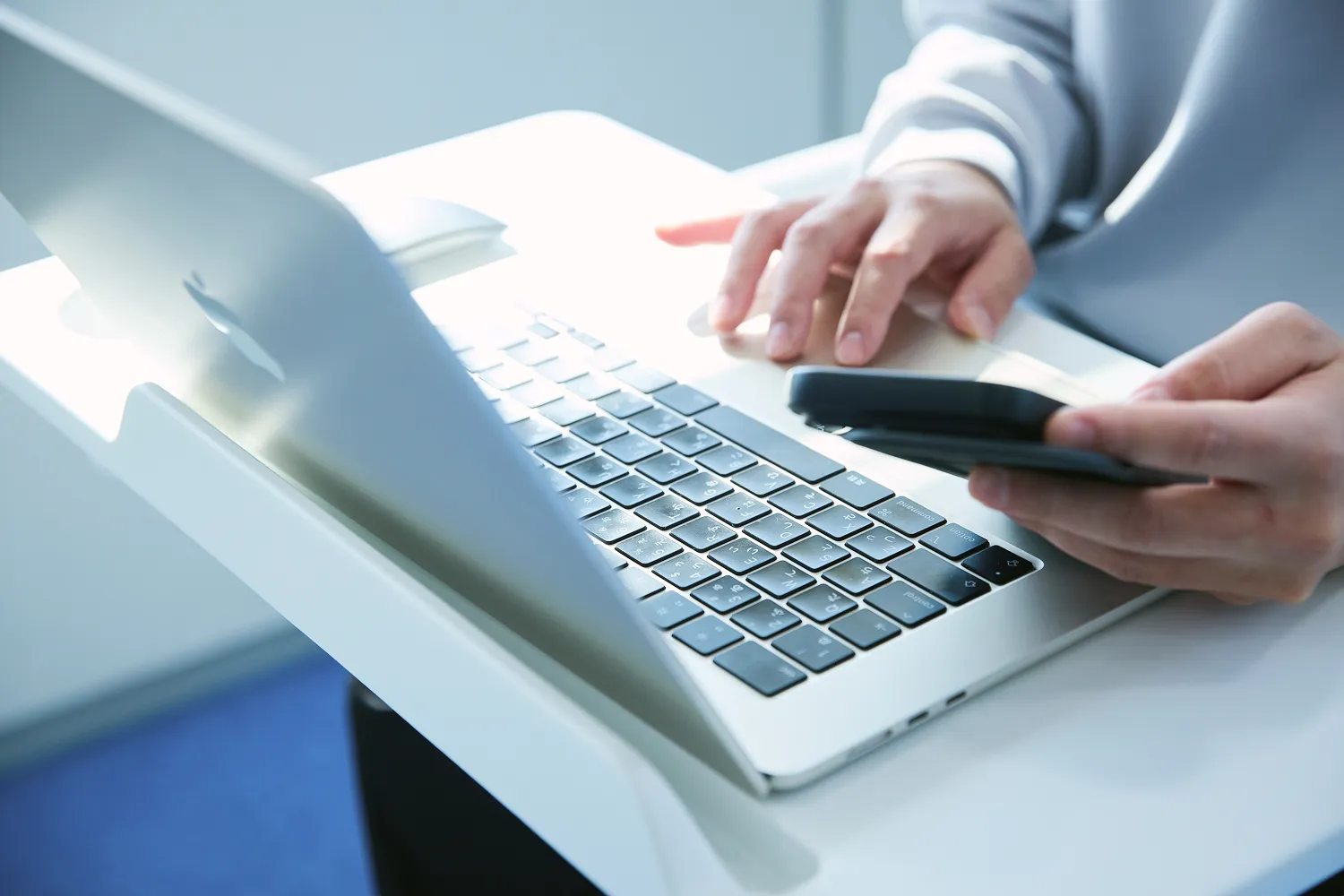 男性社員が左手にスマートフォン、右手でPCを操作しながらデザインを確認している写真