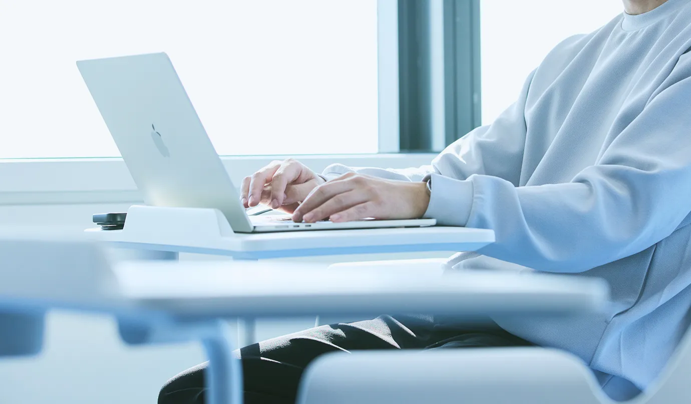 テーブル付きチェアに座り、パソコンで仕事をしている男性社員の写真