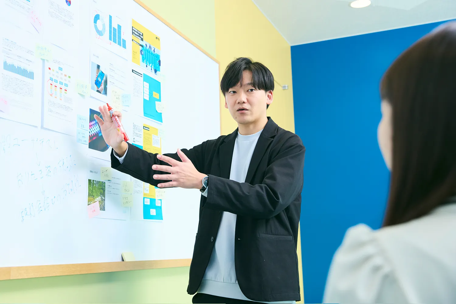 ホワイトボードの前で資料を指し示しながら説明する男性社員の写真