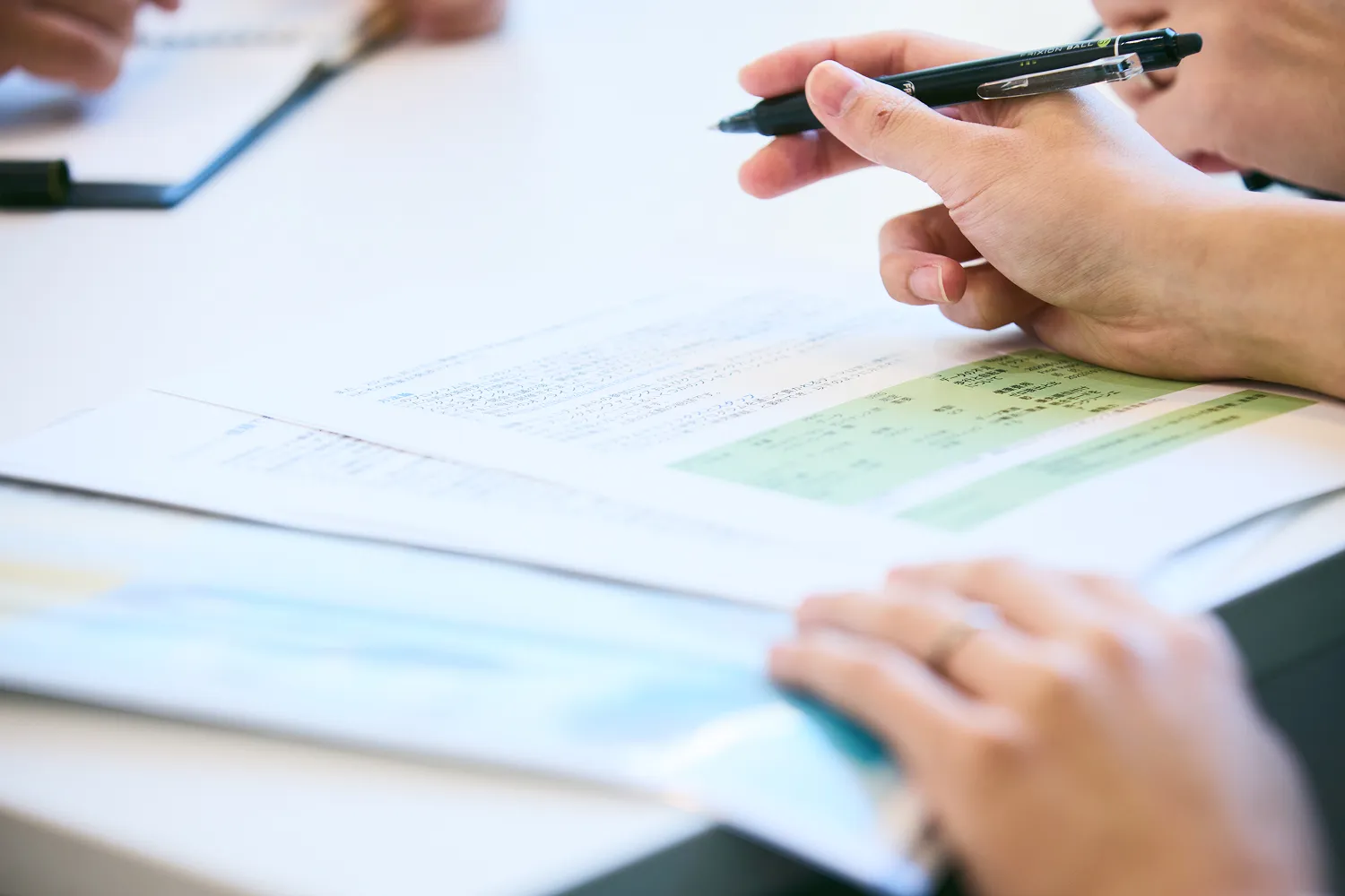 ペンを手に持ち、机に広げた資料を読み込む社員の手元の写真