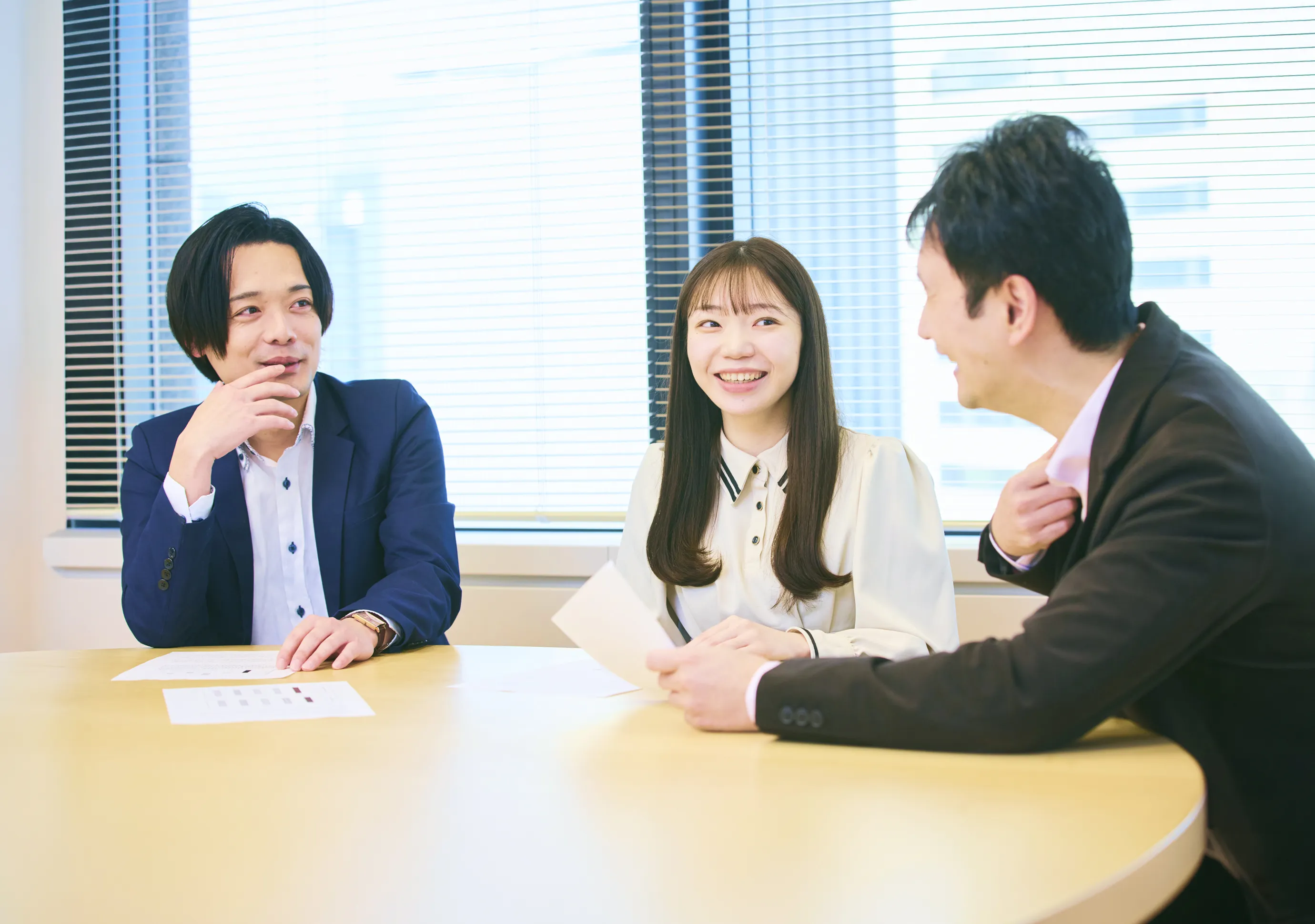 アプリケーションエンジニア G.H.さん、R.W.さん、M.F.さんがリフレッシュスペース（共有エリア）のテーブルで話をしている写真。