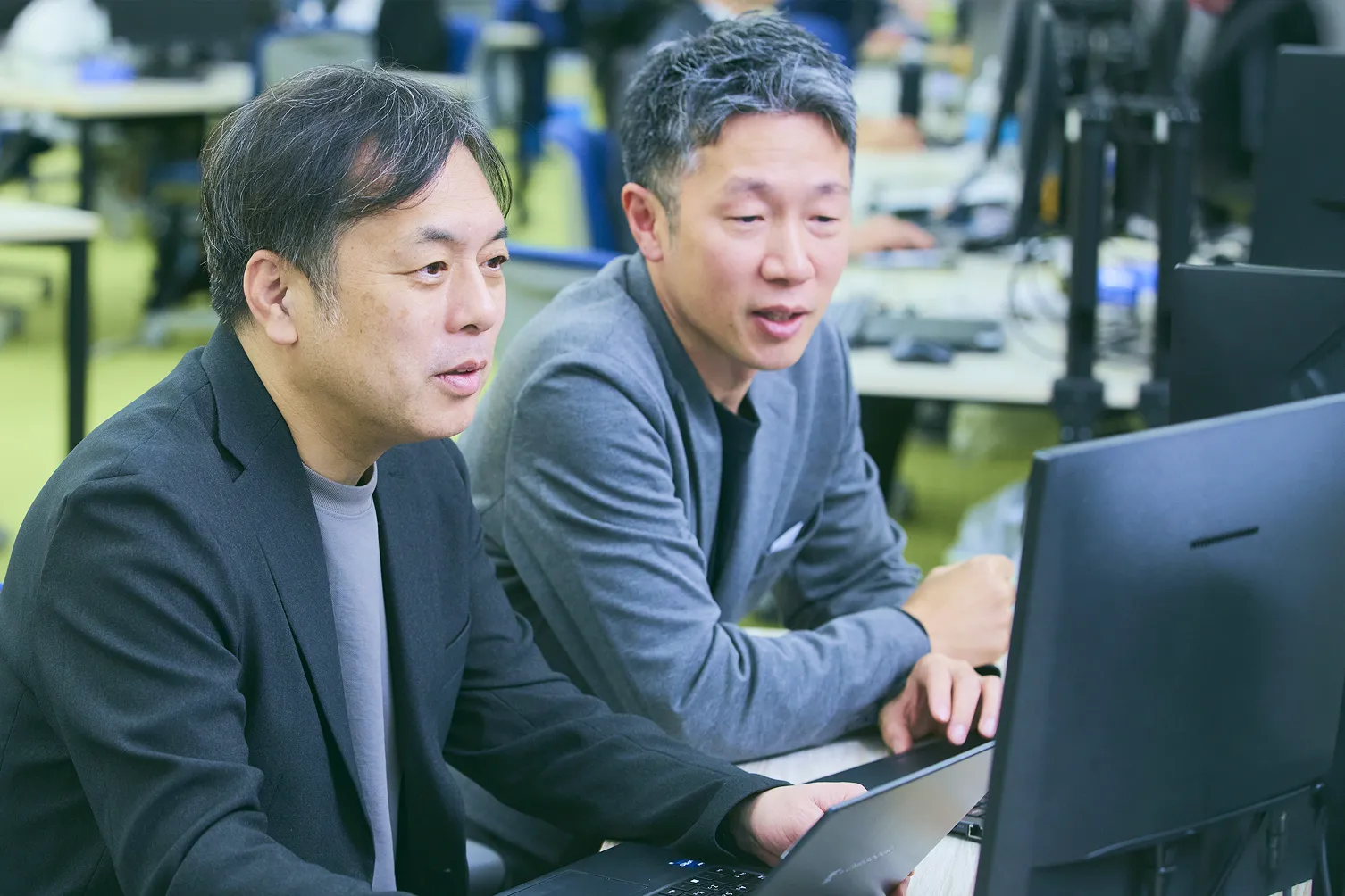 チーム統括 T.K.さんがスクラムマスター K.S.さんとモニターを確認しながら話をしている写真