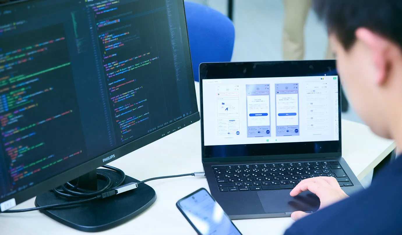 PCで書いたプログラムコードの挙動をスマートフォンを片手に検証している写真