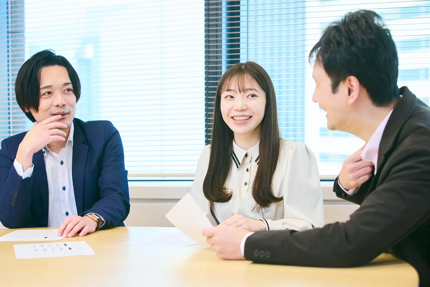 男性社員2名と女性社員1名がリフレッシュスペース（共有エリア）のテーブルで話をしている写真