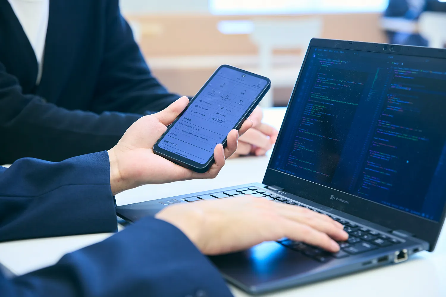 PCで書いたプログラムコードの挙動をスマートフォンを片手に検証している写真
