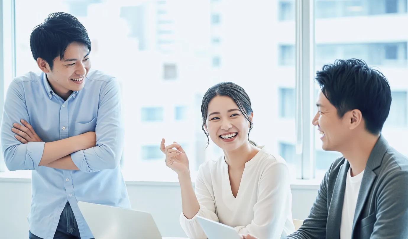 オフィスでノートパソコンを囲み会話する3人の社員の写真