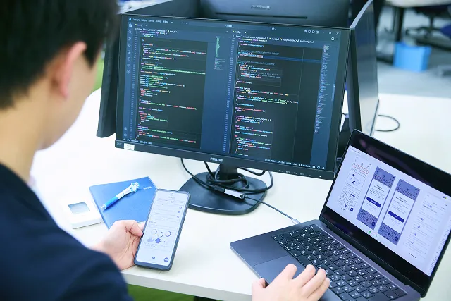 男性社員と女性社員がそれぞれPCに向かってプログラミングしている写真。