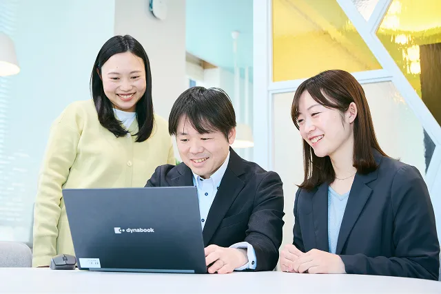 若手女性社員2人と若手男性社員1人が、PCを見ながら議論をしている写真。